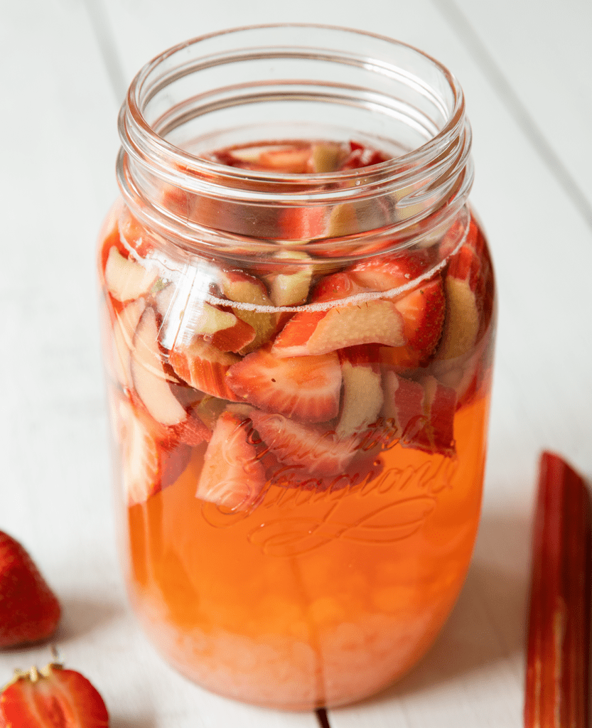 Nahaufnahme Gärgefäß mit einem Rhabarber-Erdbeer-Wasserkefir, frischem Rhabarber und Erdbeeren